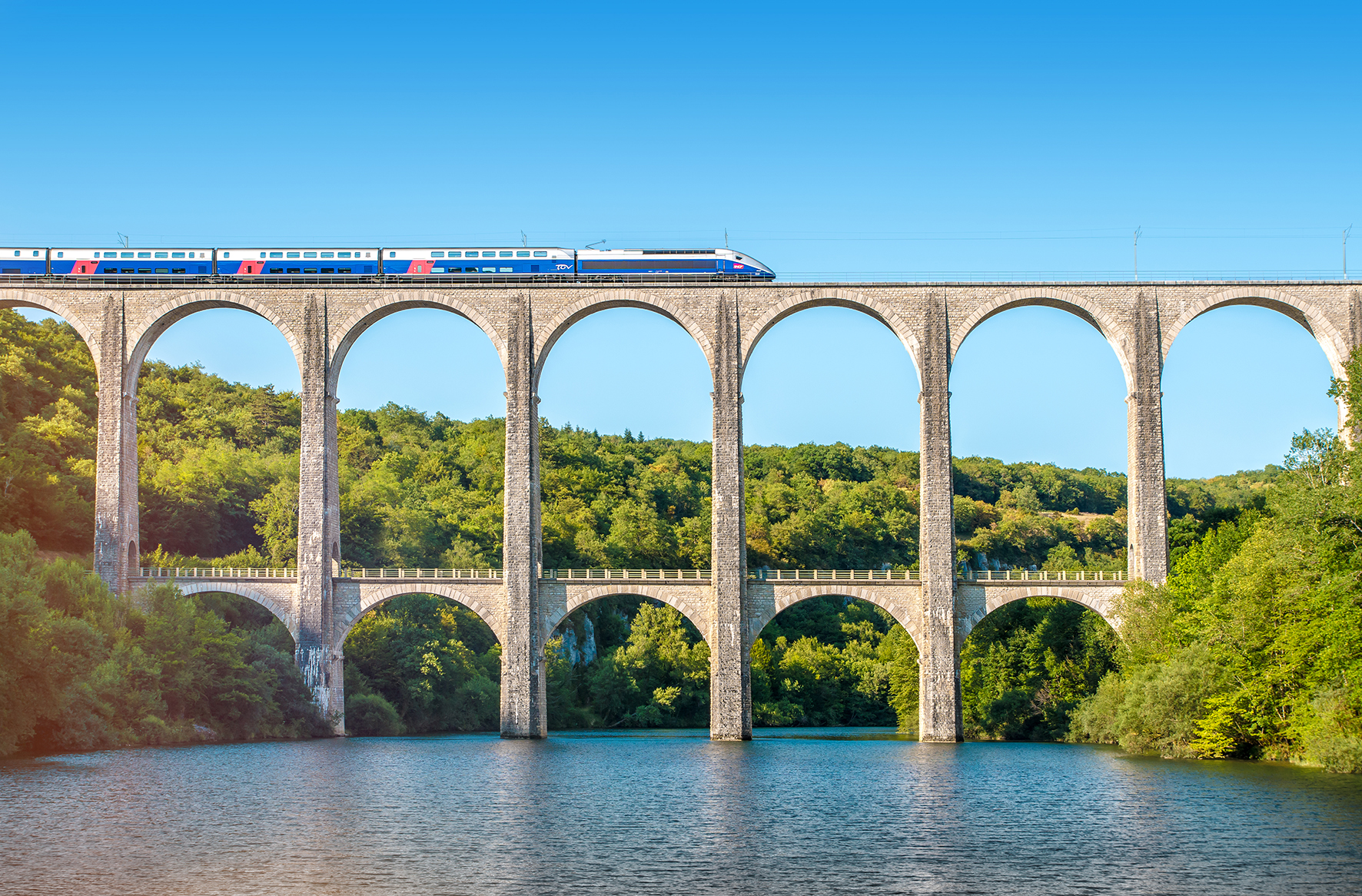TGV fährt auf einem Viadukt, das sich über einen Fluss erstreckt.