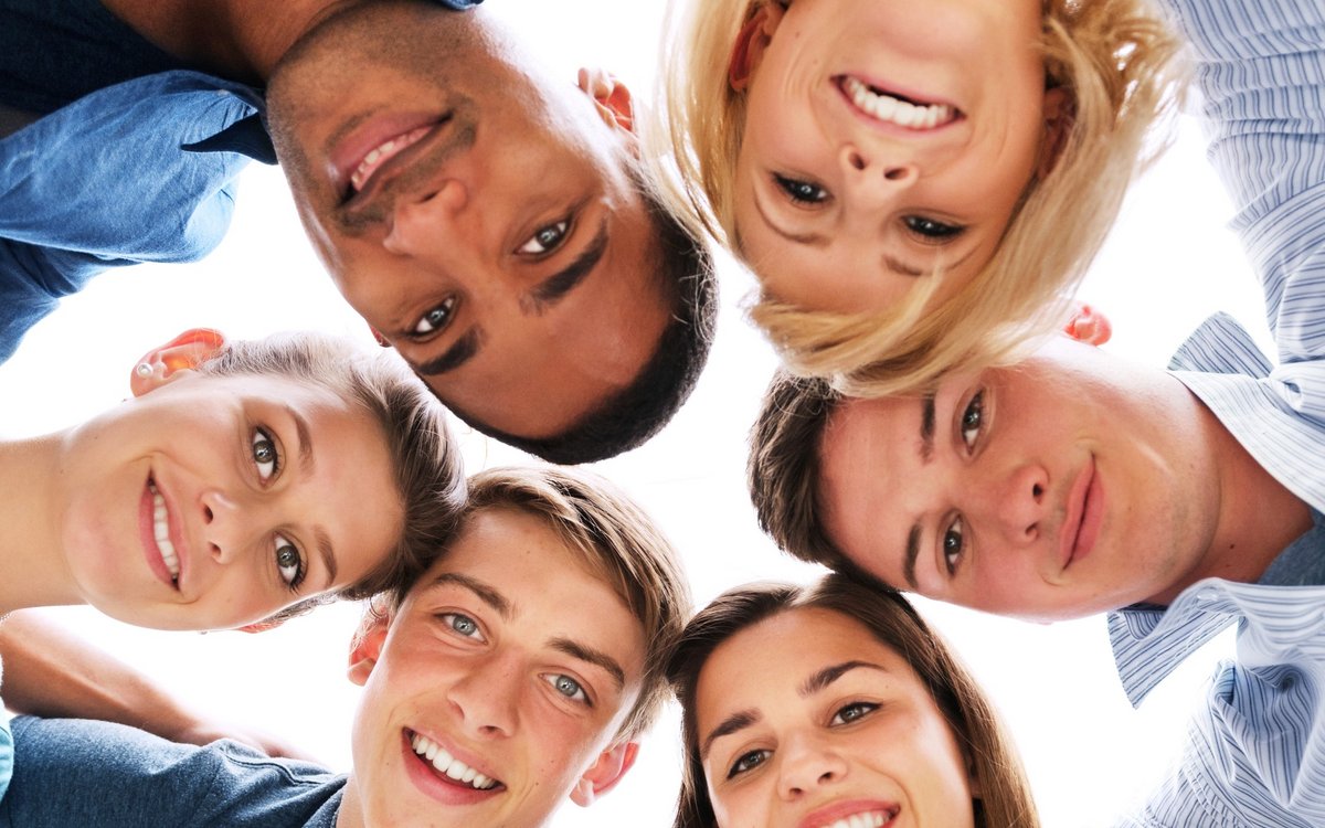 laughing young people stand in a circle and put their faces together, seen from below