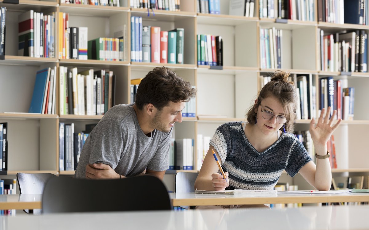 two students sitting at a table in front of bookshelves