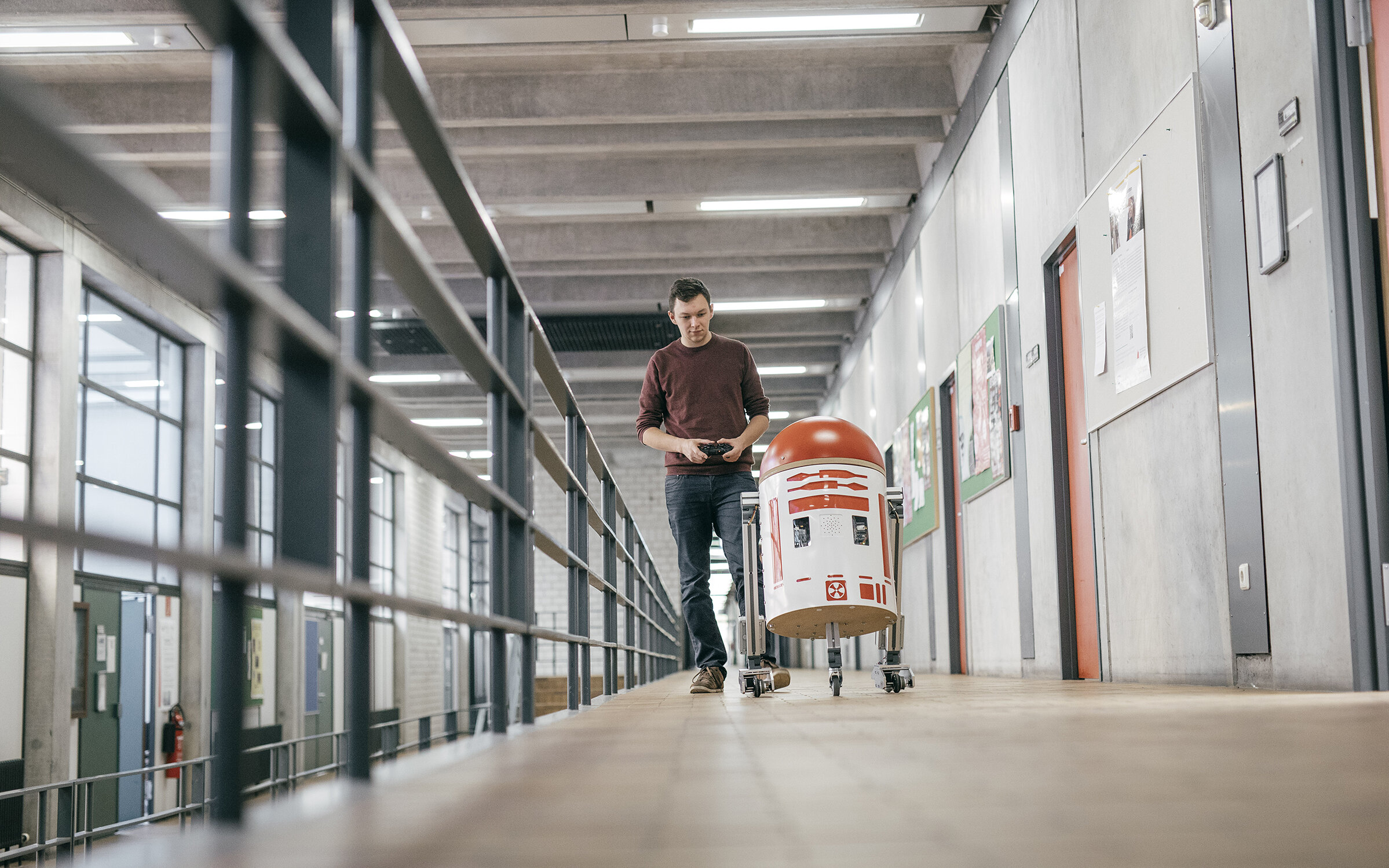 student moves a homemade robot by remote control along a hallway