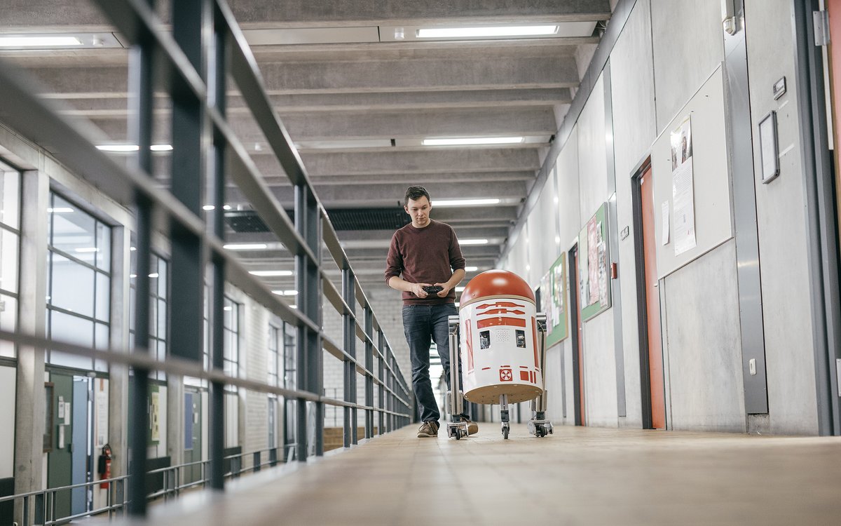 student moving a robot by remote control along the hallway in the lab wing