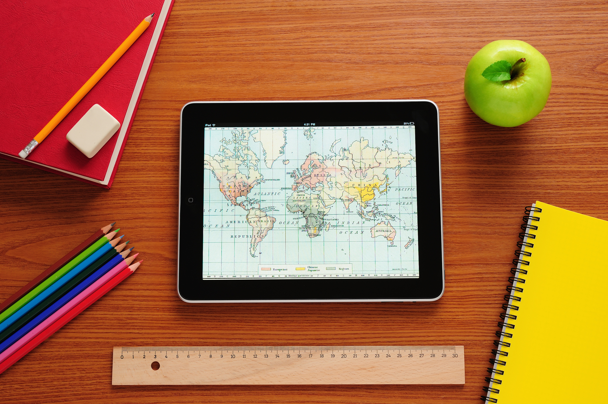 Tablet, eine Website mit Weltkarte geöffnet, und weitere Schulutensilien auf einem Tisch liegend