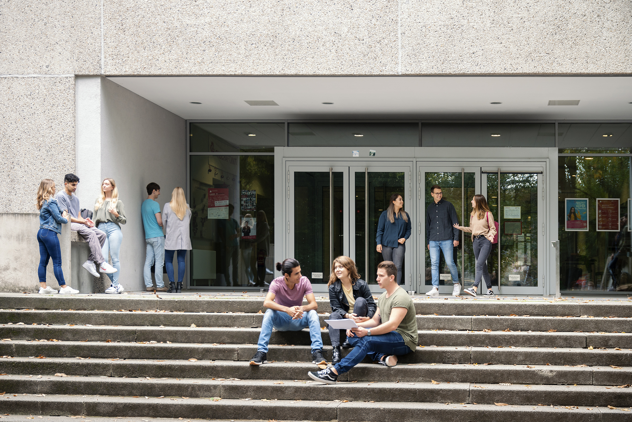 students standing or sitting on the stairs in front of a HKA building