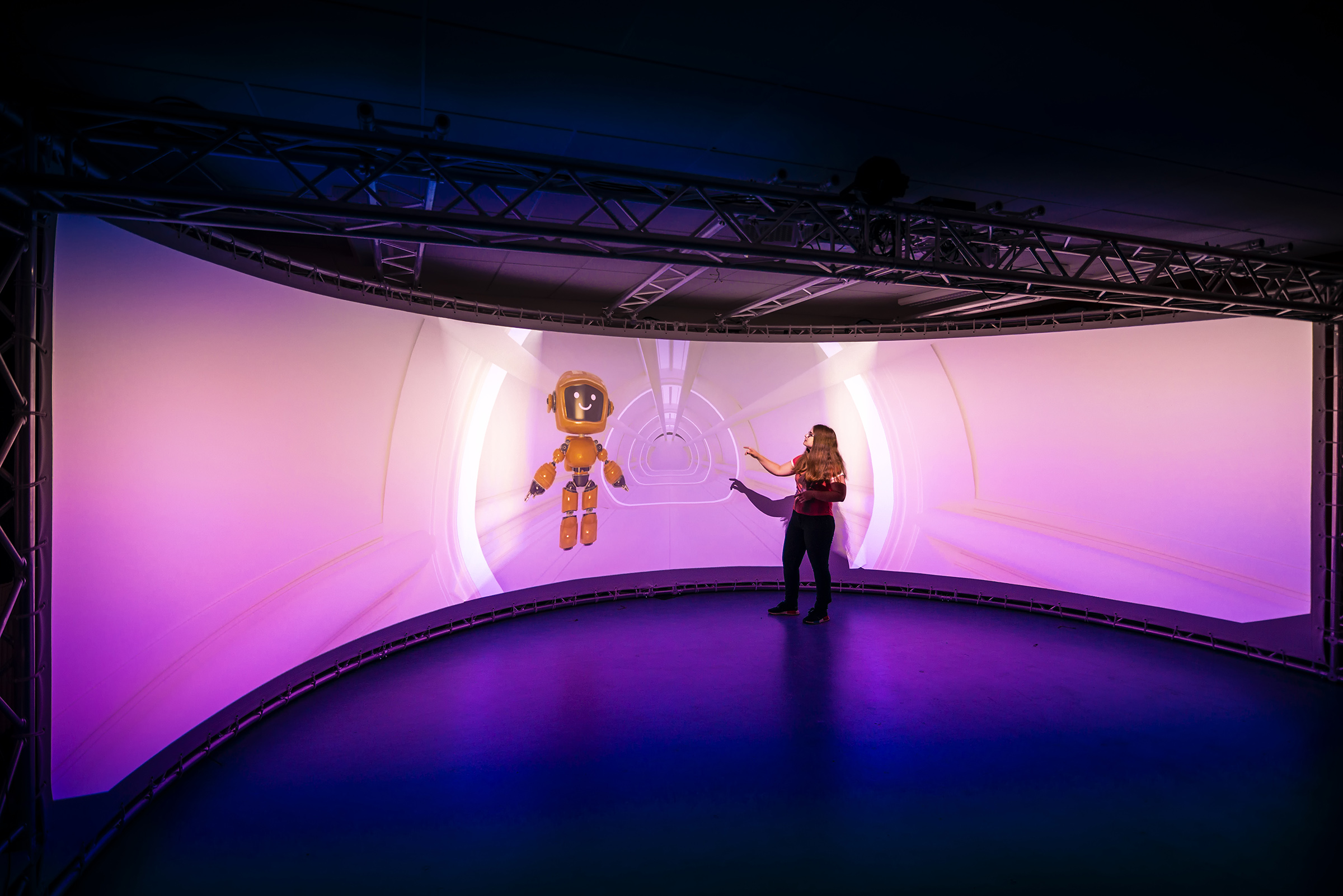 young woman in front of semicircular floor-to-ceiling screen with robot on it
