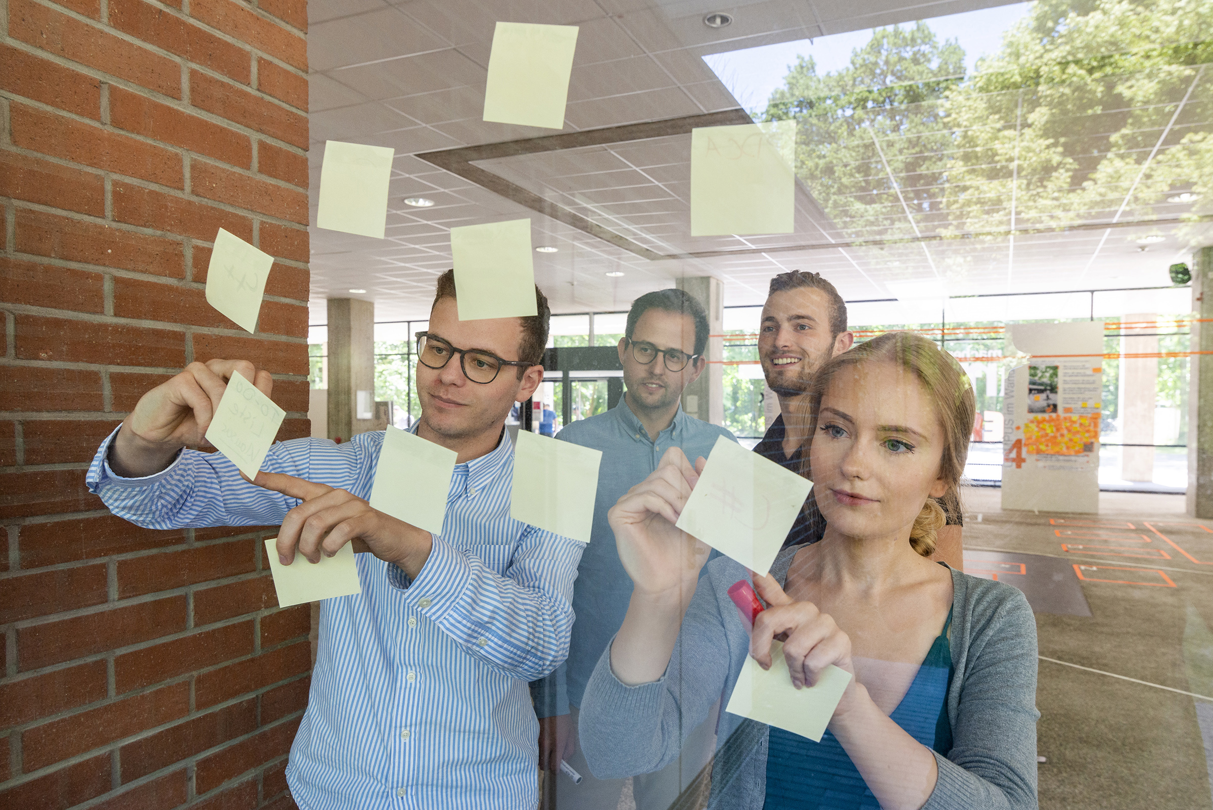 glass wall with young people standing behind and putting memo stickers on it