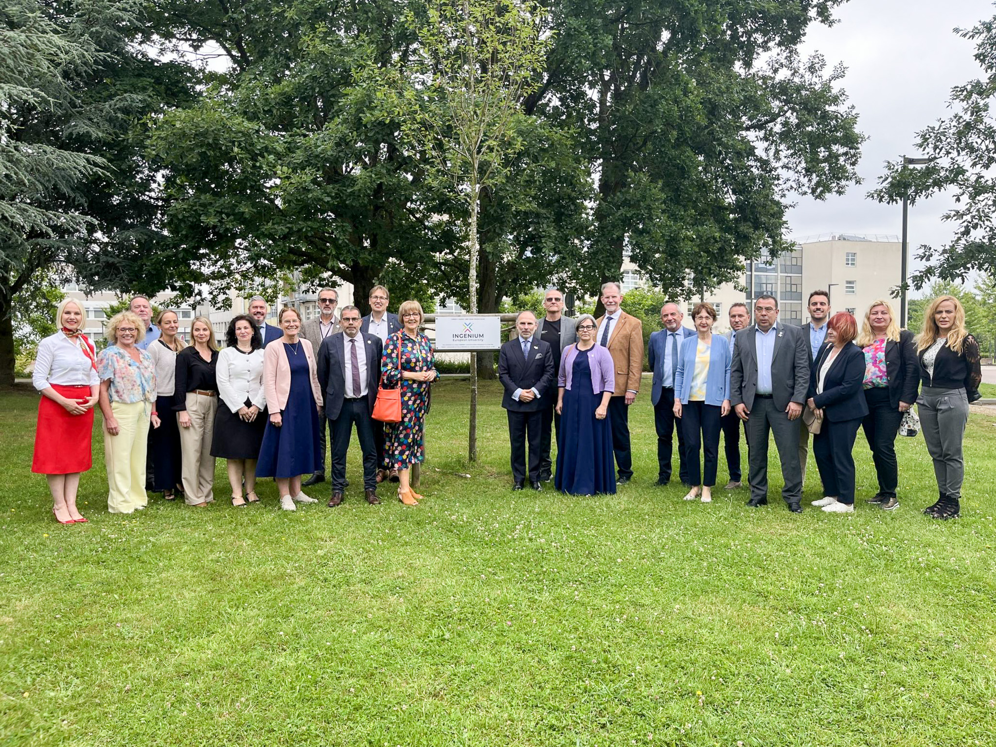 Gruppe von etwa zwanzig Personen in Businesskleidung steht auf einer Rasenfläche vor einem Schild mit dem INGENIUM-Logo und Bäumen im Hintergrund – Teilnehmende des INGENIUM-Allianzrats in Rouen, Juni 2026.