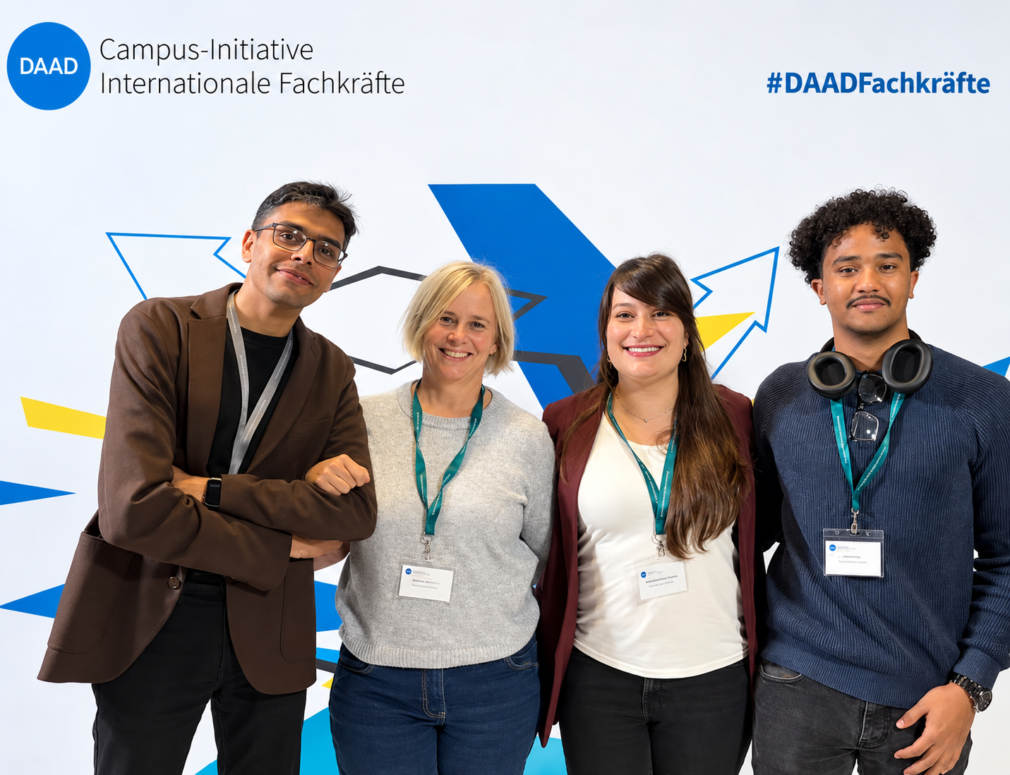 Vier Personen stehen nebeneinander vor einer Fotowand der DAAD-Campus-Initiative „Internationale Fachkräfte“ und lächeln in die Kamera.