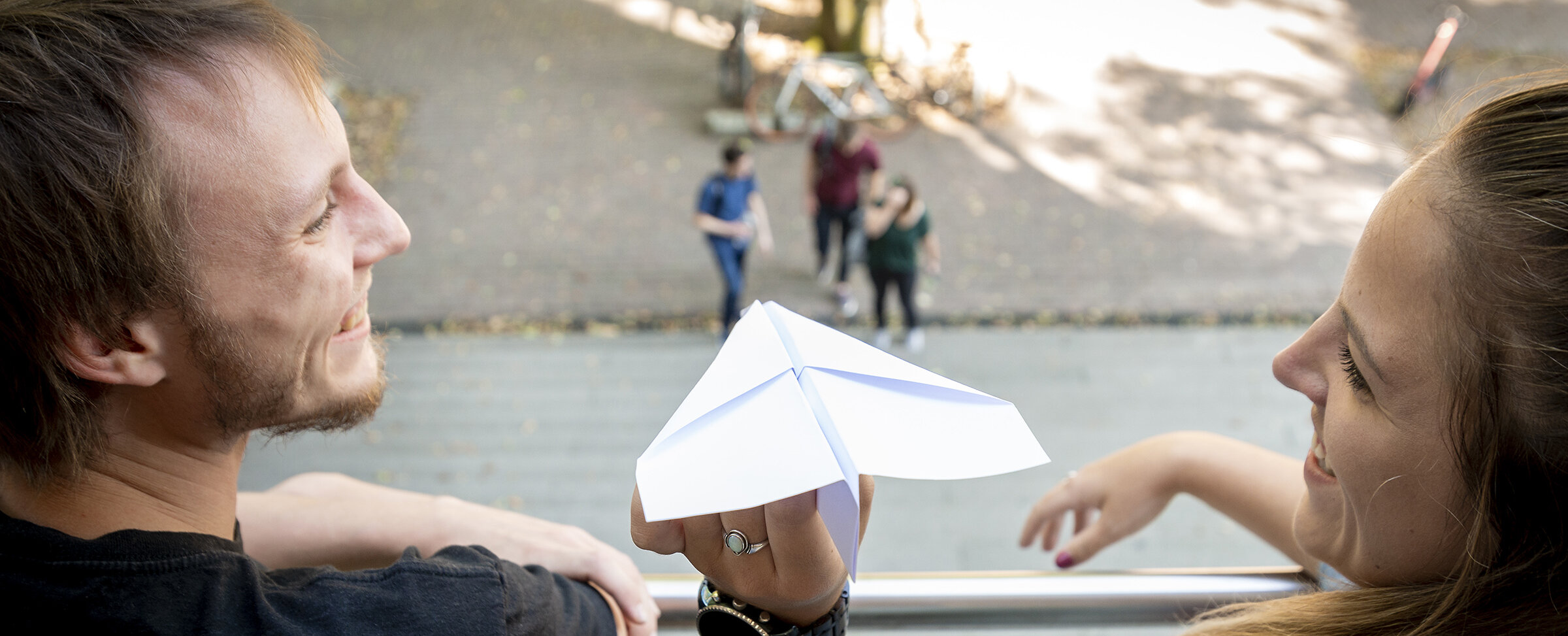 two students on a balcony, about to let fly a paper plane