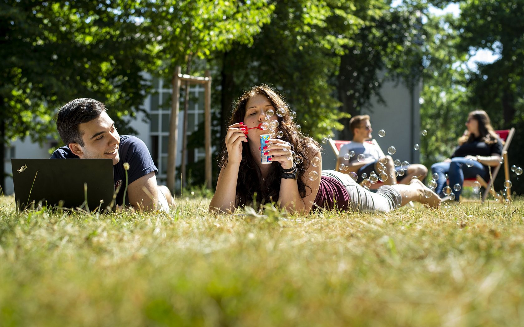 young people lying on the grass on campus enjoy the sunshine and blowing soap bubbles