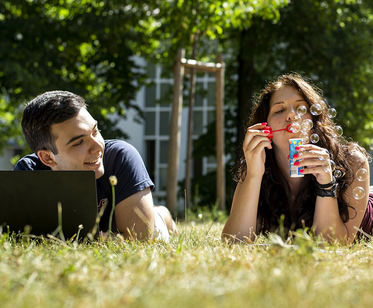 two students lying on the grass at HKA campus, one of them blowing soap bubbles