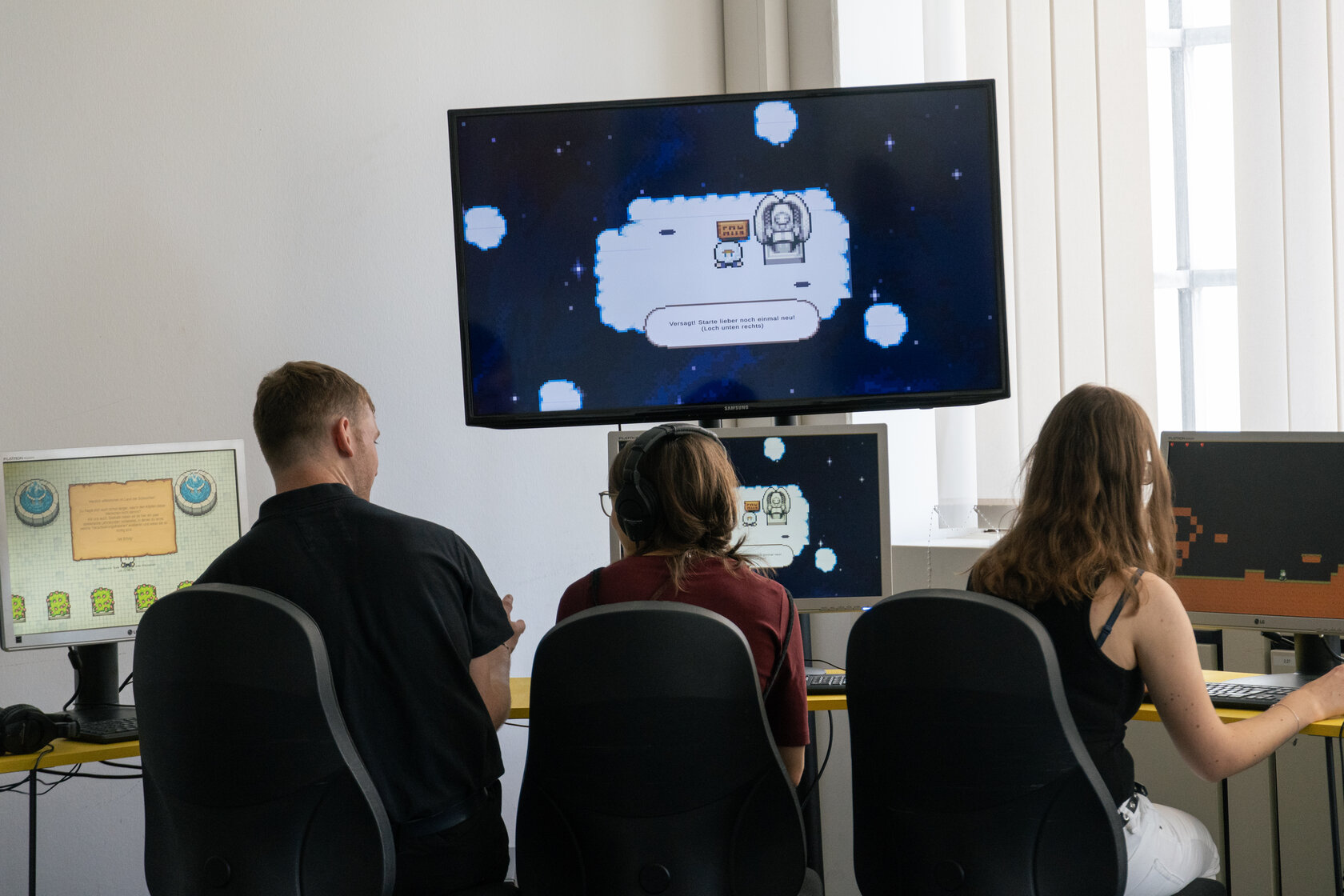 3 Personen sitzen vor mehreren Bildschirmen und spielen das Computerspiel „Schwurbler Run“ von Leon Günther, Julius Meyer, Lam Vu, Joel Döffinger