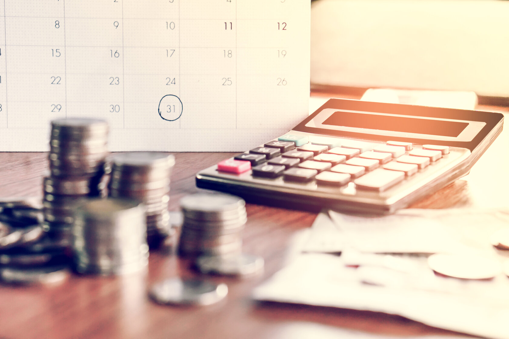 view of a desktop with pocket calculator, stacks of coins, and calendar view of a desktop with pocket calculator, stacks of coins, and calendar