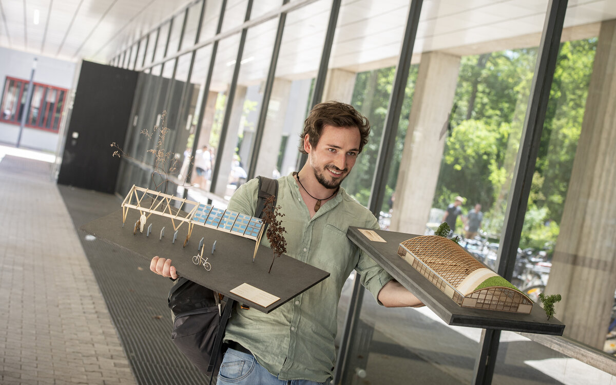 Studierender der Fakultät Architektur und Bauwesen mit Modell vor dem B-Bau 