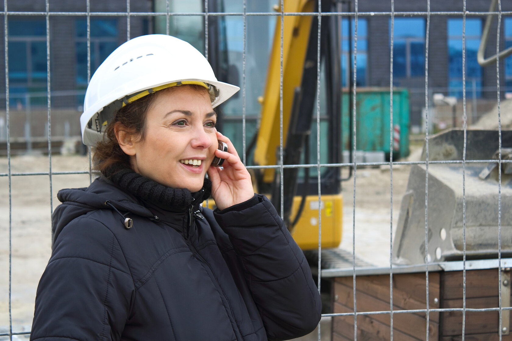 young woman wearing a hard hat and talking into a mobile phone on a construction site