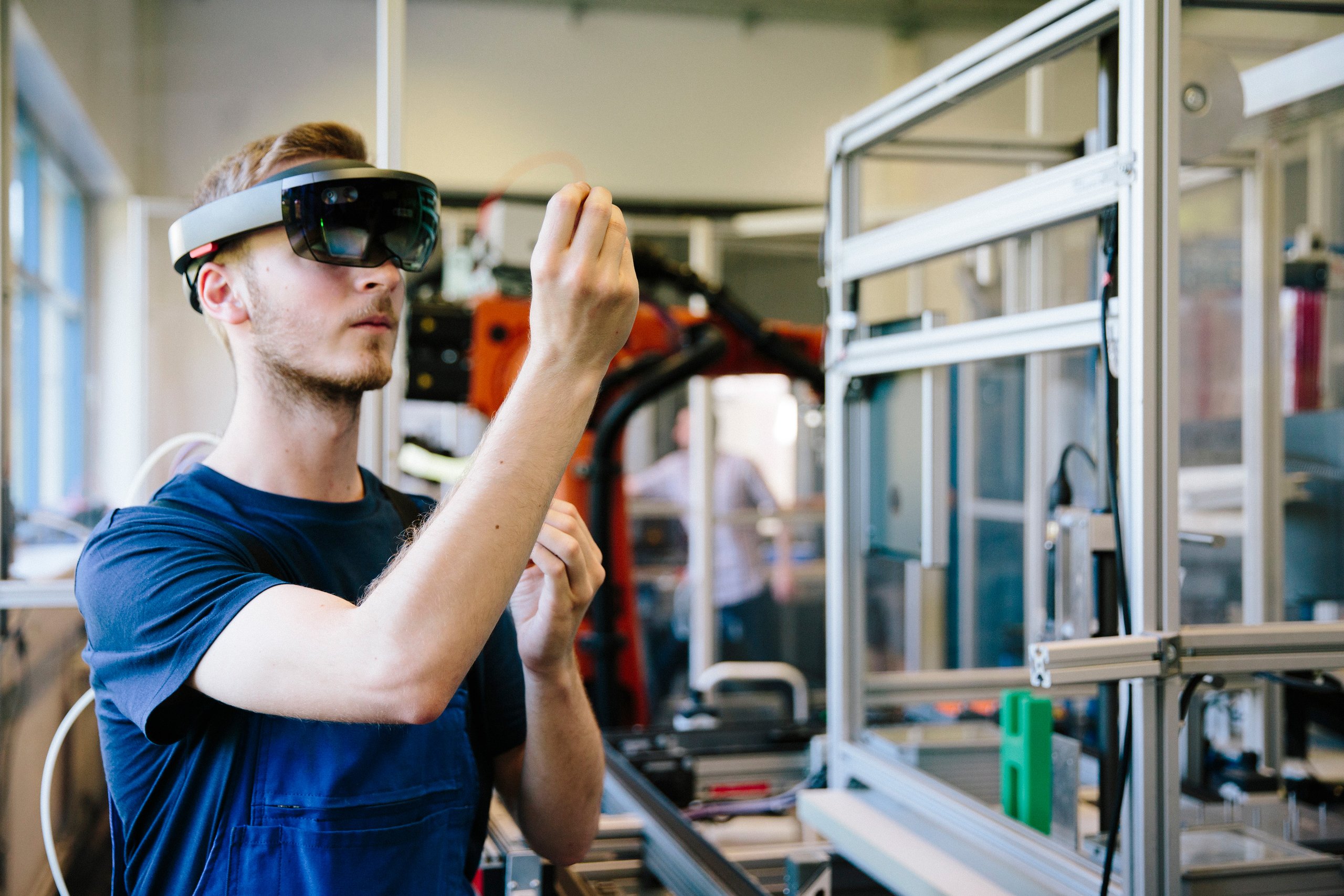 student in the lab, wearing VR goggles, with industrial robot in the background