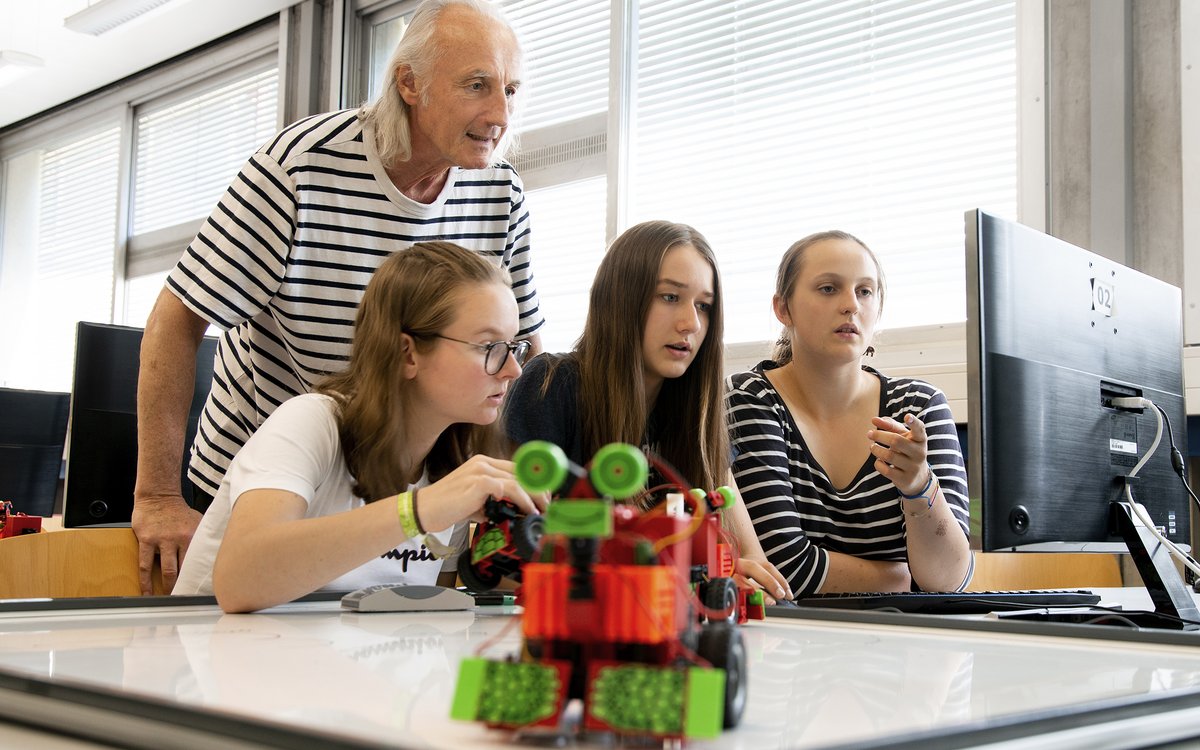 young women and professor at laptop, with small robot sitting on the desk