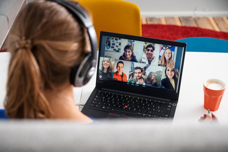 Frau schaut auf einen PC, wo eine Videokonferenz stattfindet. 