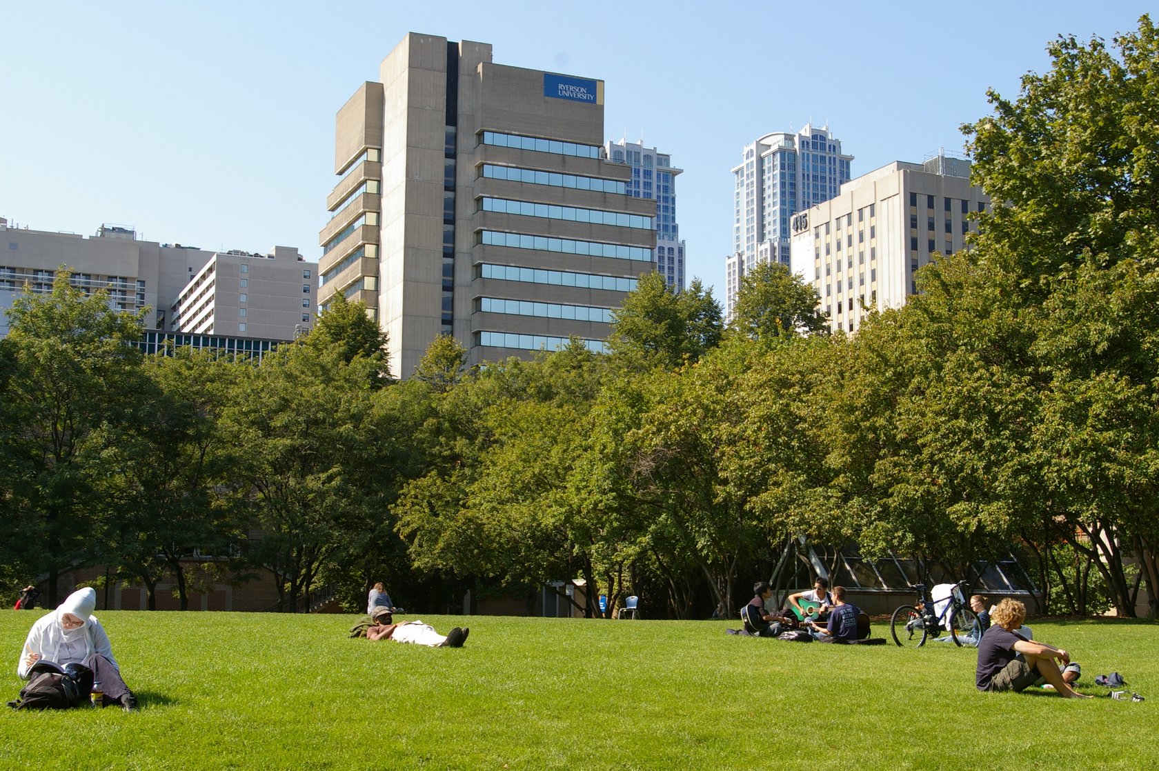 students on lawn, surrounded by trees and highrise-buildings