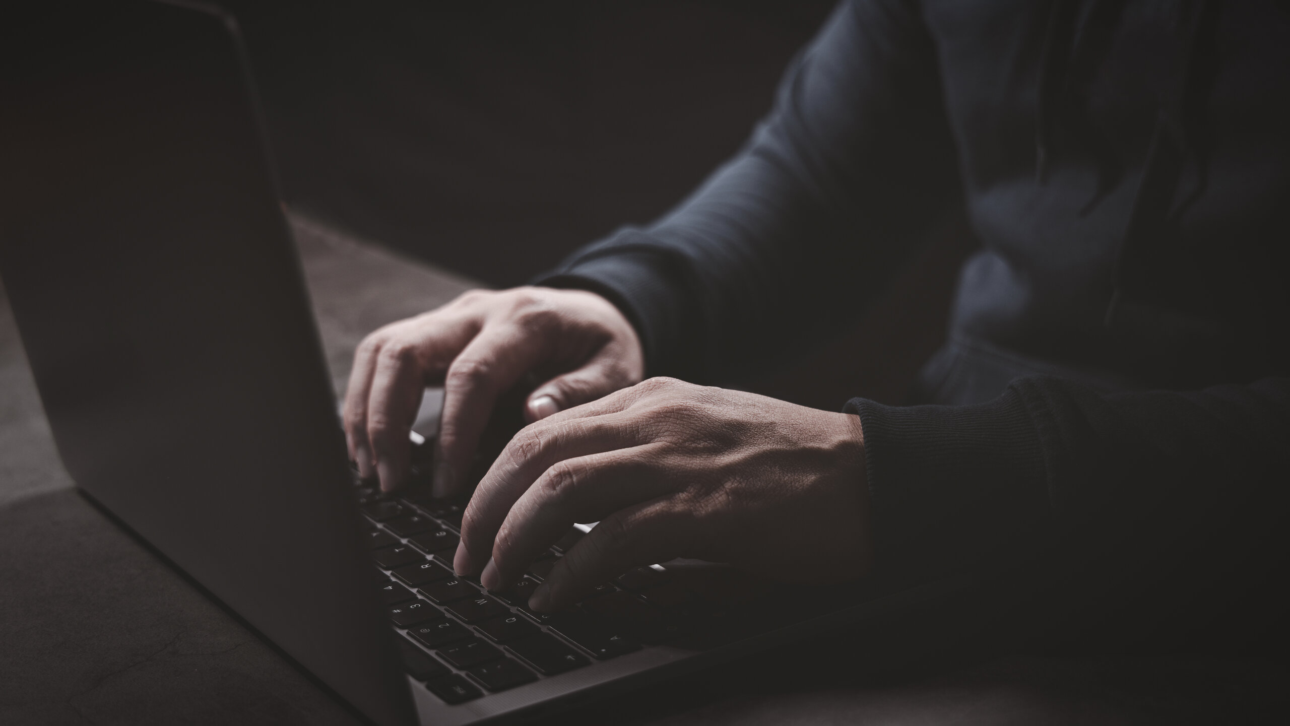 Männerhände tippen in dunkler Umgebung auf der Tastatur eines Laptops
