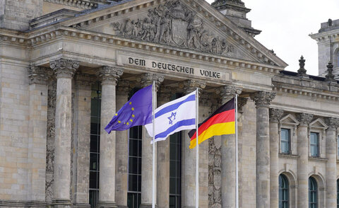 Blick auf den Eingangsbereich des Reichstagsgebäudes in Berlin. Vor dem Säulenportal wehen drei Flaggen: die blaue EU-Flagge mit goldenen Sternen, die weiß-blaue israelische Flagge mit dem Davidstern sowie die schwarz-rot-goldene Deutschlandfahne.