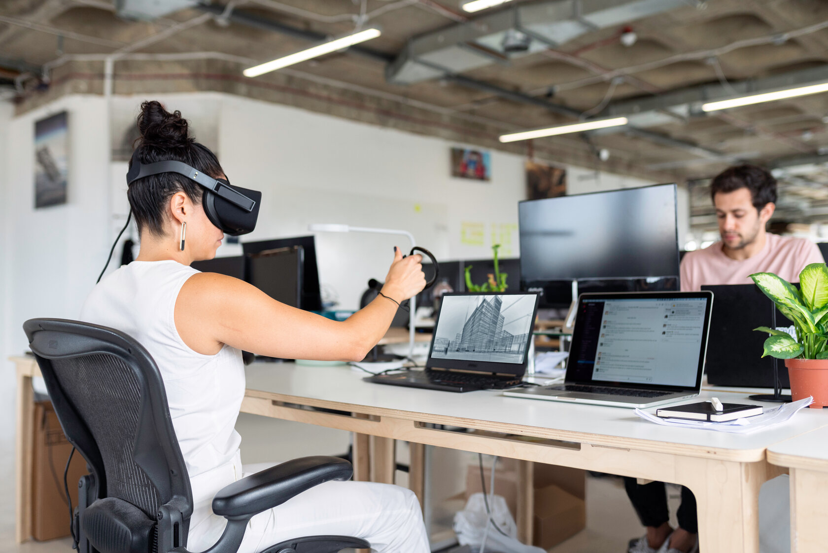 two students sit in a pool room with computer workstations, one of them wearing VR goggles two students sit in a pool room with computer workstations, one of them wearing VR goggles