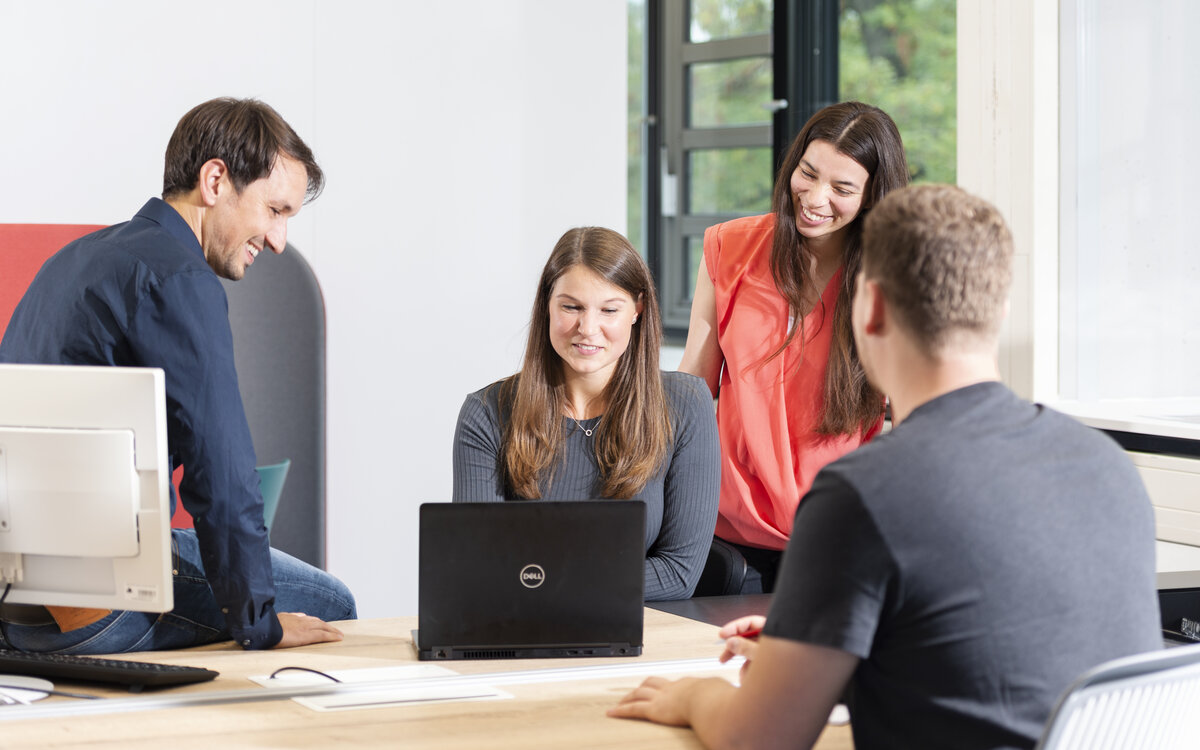 Dozent und 3 Studierende am Schreibtisch in Interaktion mit Notebook