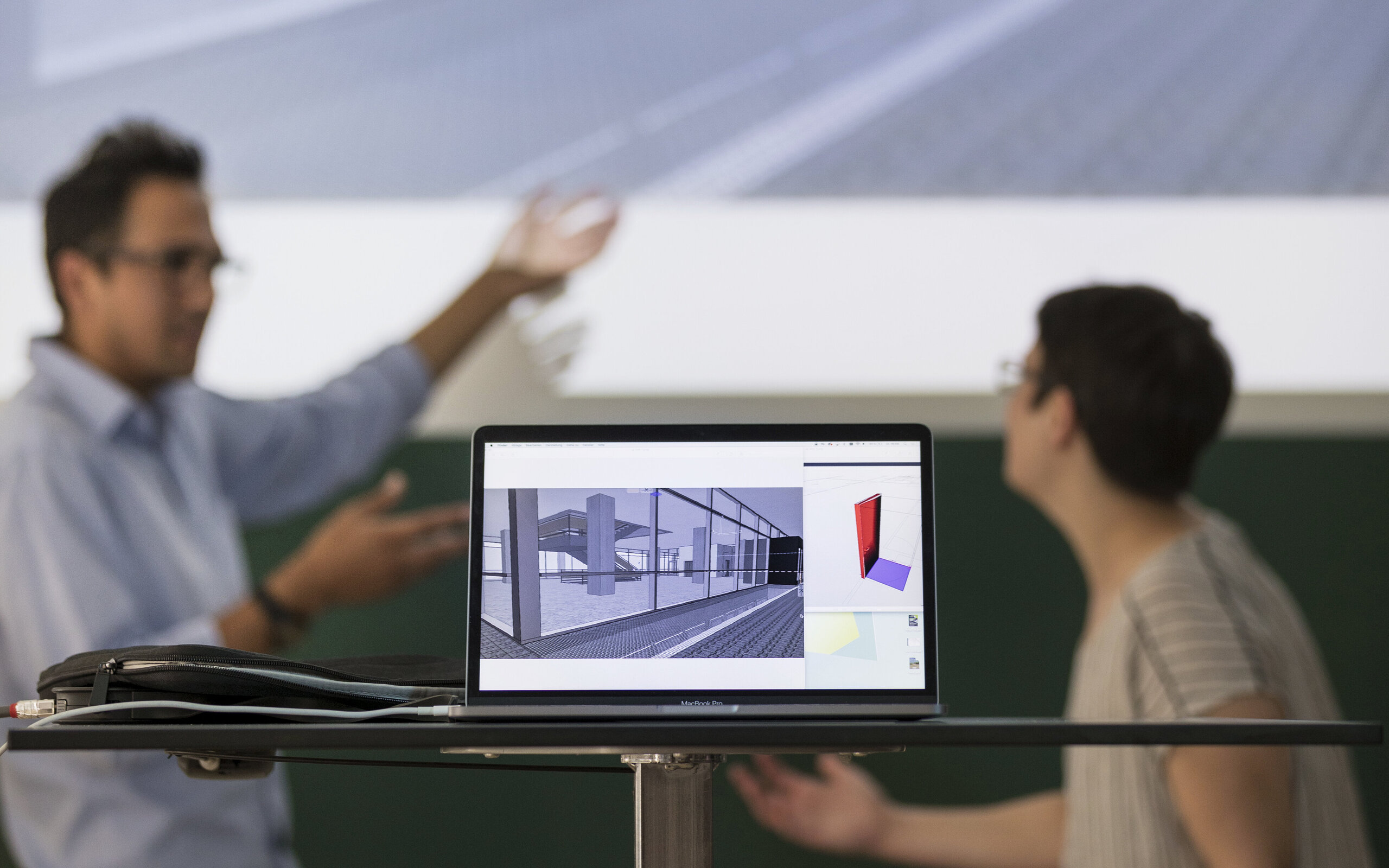 in the foreground a laptop with a building draft, in the background two people discussing