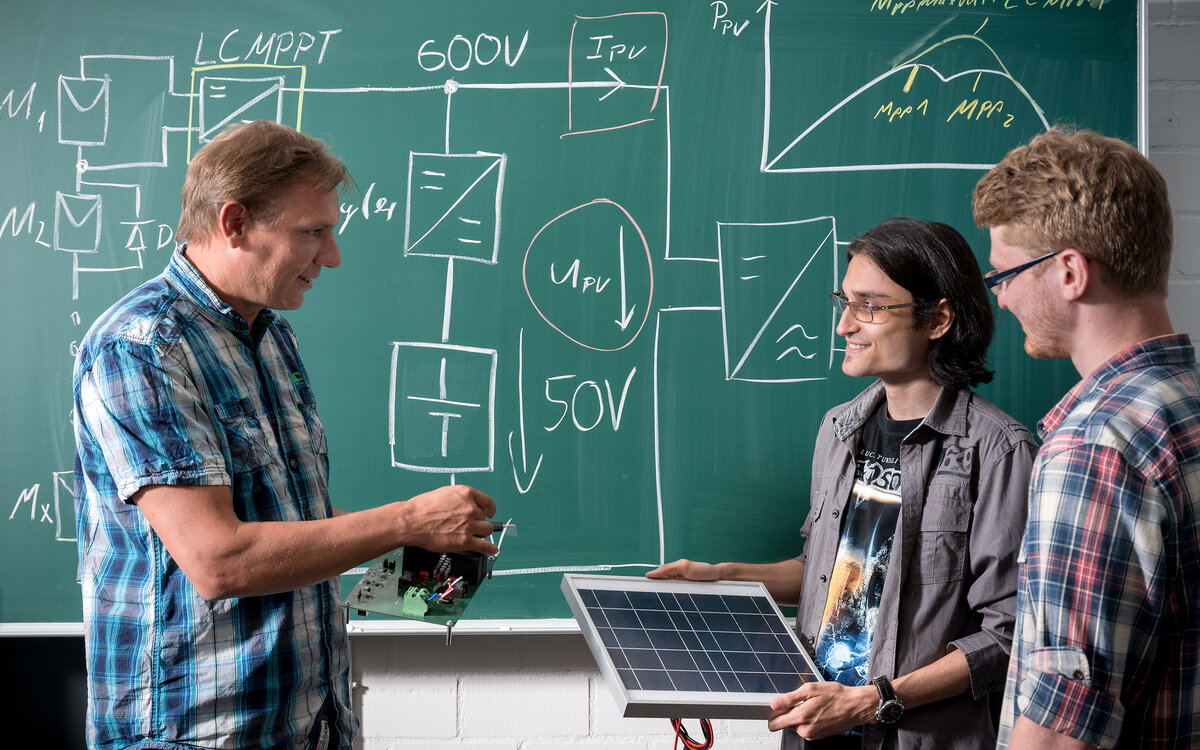 teacher in front of blackboard talking to two students