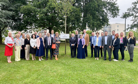 Gruppe von etwa zwanzig Personen in Businesskleidung steht auf einer Rasenfläche vor einem Schild mit dem INGENIUM-Logo und Bäumen im Hintergrund – Teilnehmende des INGENIUM-Allianzrats in Rouen, Juni 2026.