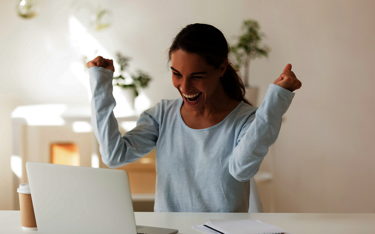 positiver Bescheid: junge Frau jubelt beim Blick auf Ihr Notebook