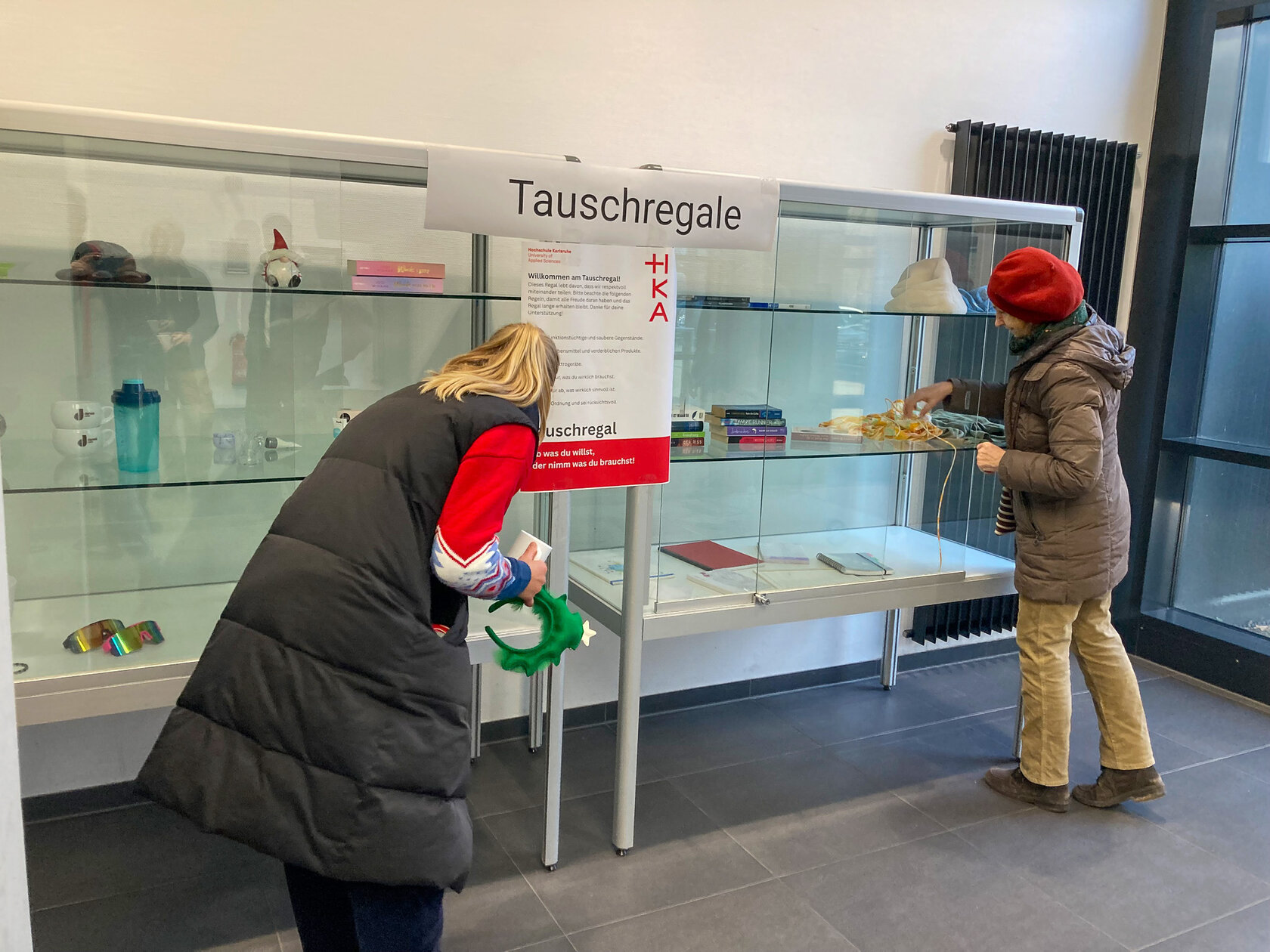 Ein Regal voller Gegenstände und zwei Personen, die es befüllen.