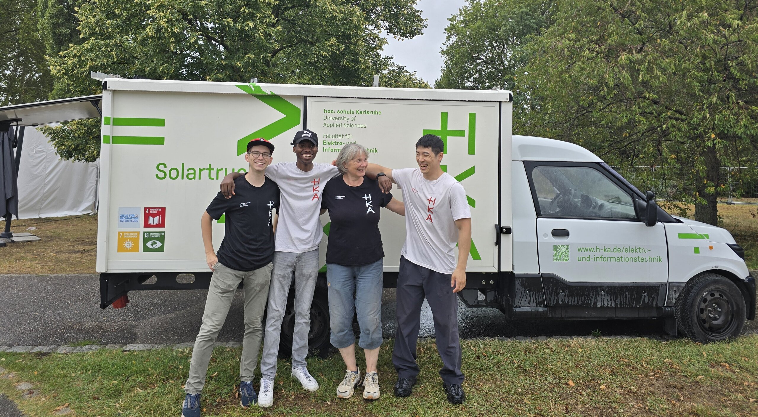 Vier Personen in HKA-T-Shirts stehen lächelnd nebeneinander vor einem weißen Fahrzeug mit der Aufschrift „Solartruck".