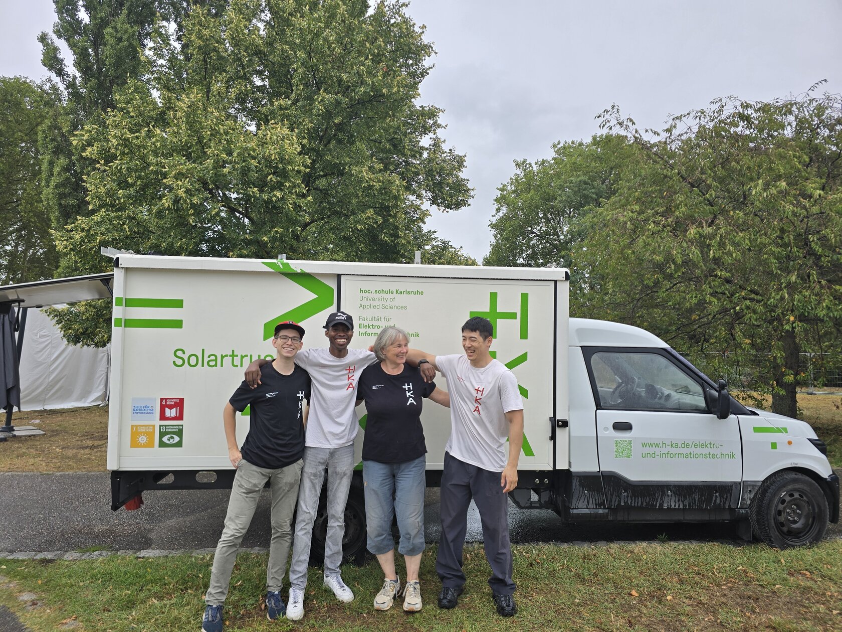 Vier Personen in HKA-T-Shirts stehen lächelnd nebeneinander vor einem weißen Fahrzeug mit der Aufschrift „Solartruck".