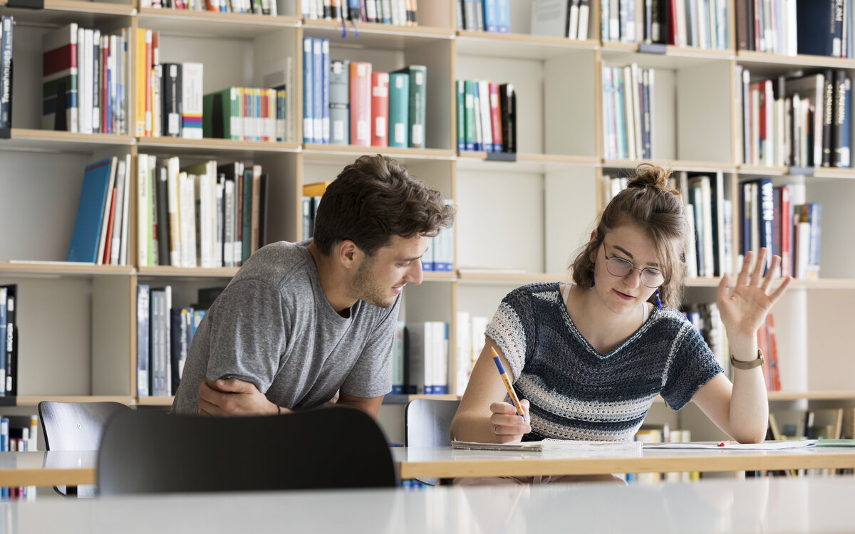 two students sitting on a table in front of bookshelves