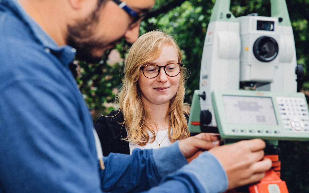 two students working with a surveying tool