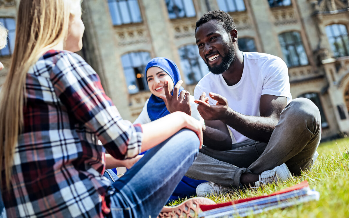 group of international students sitting on the grass in front of a university building