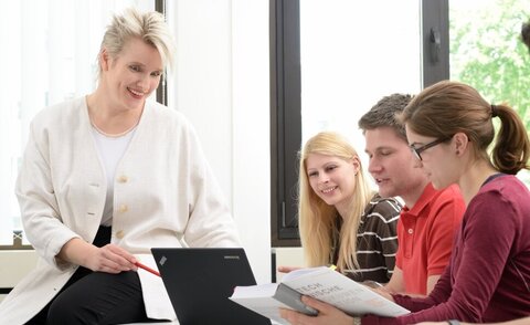 Professorin am Tisch mit einer Gruppe Studierenden