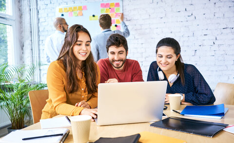 Group of young creative workers looking at laptop and brainstorming during meeting. University students studying together