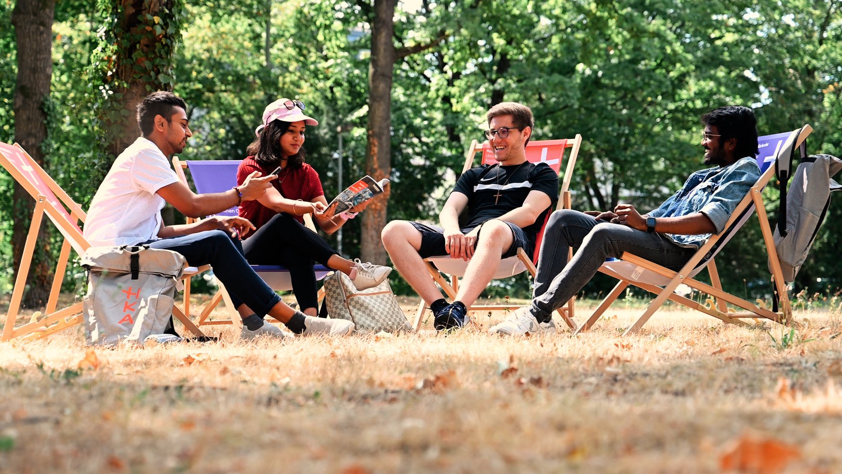 Vier internationale Studierende sitzen auf Liegestühlen im Park und unterhalten sich. 