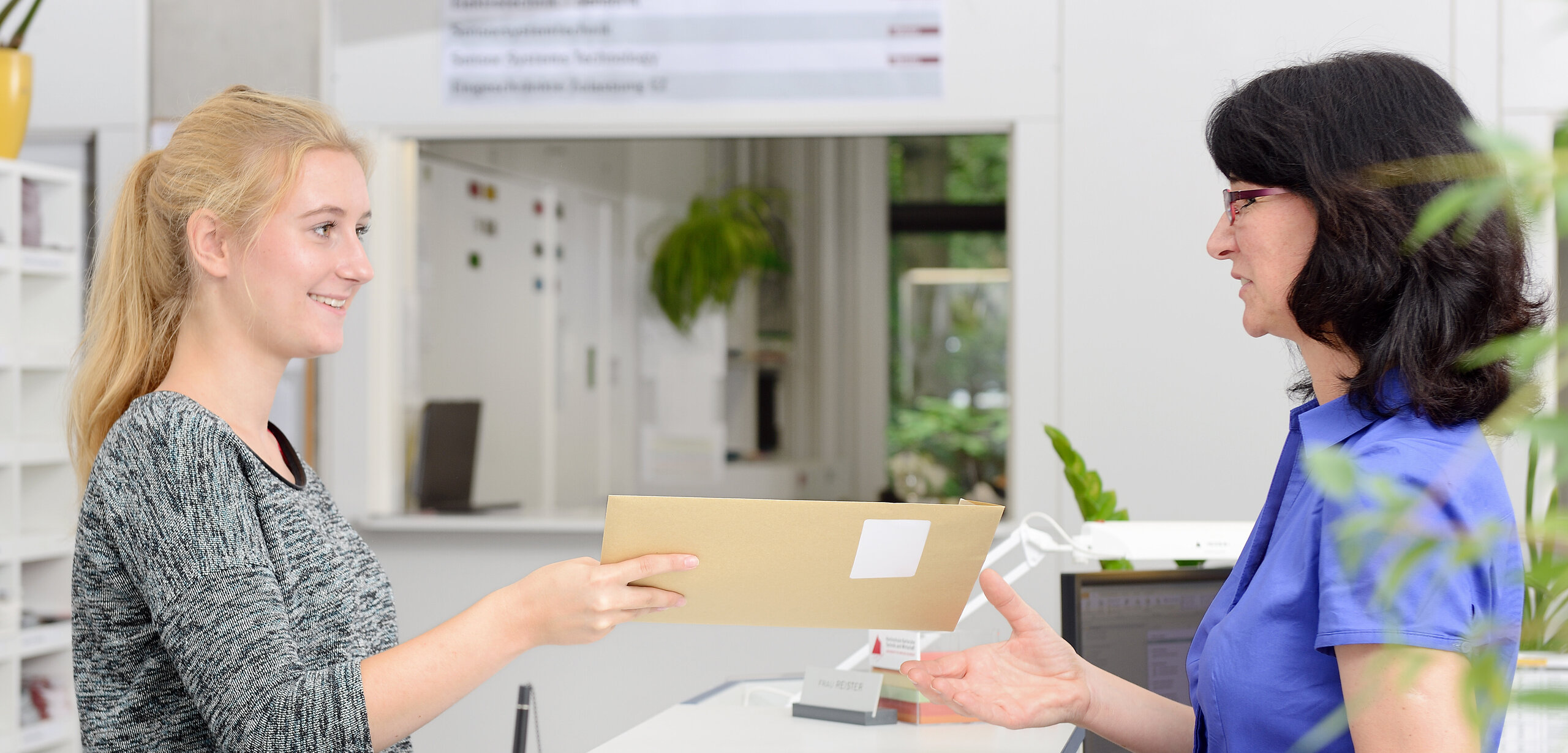 applicant hands over an envelope to the Student Registry responsible