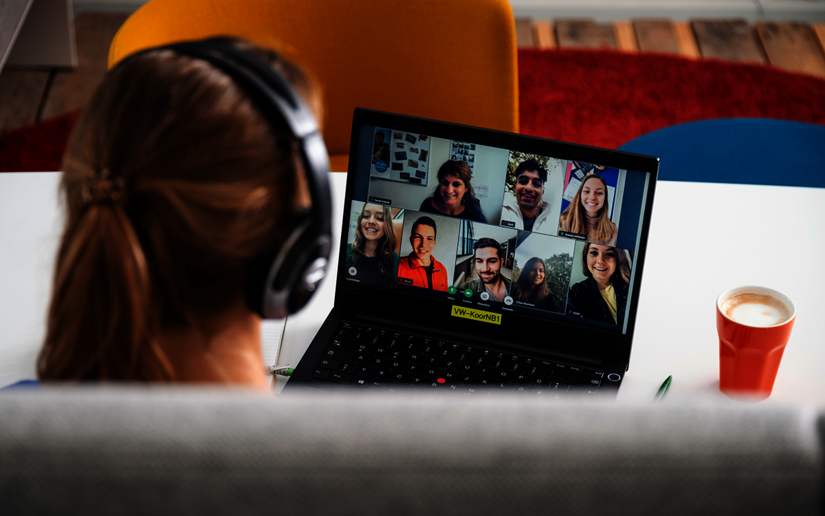 Frau schaut auf einen PC, wo eine Videokonferenz stattfindet. 
