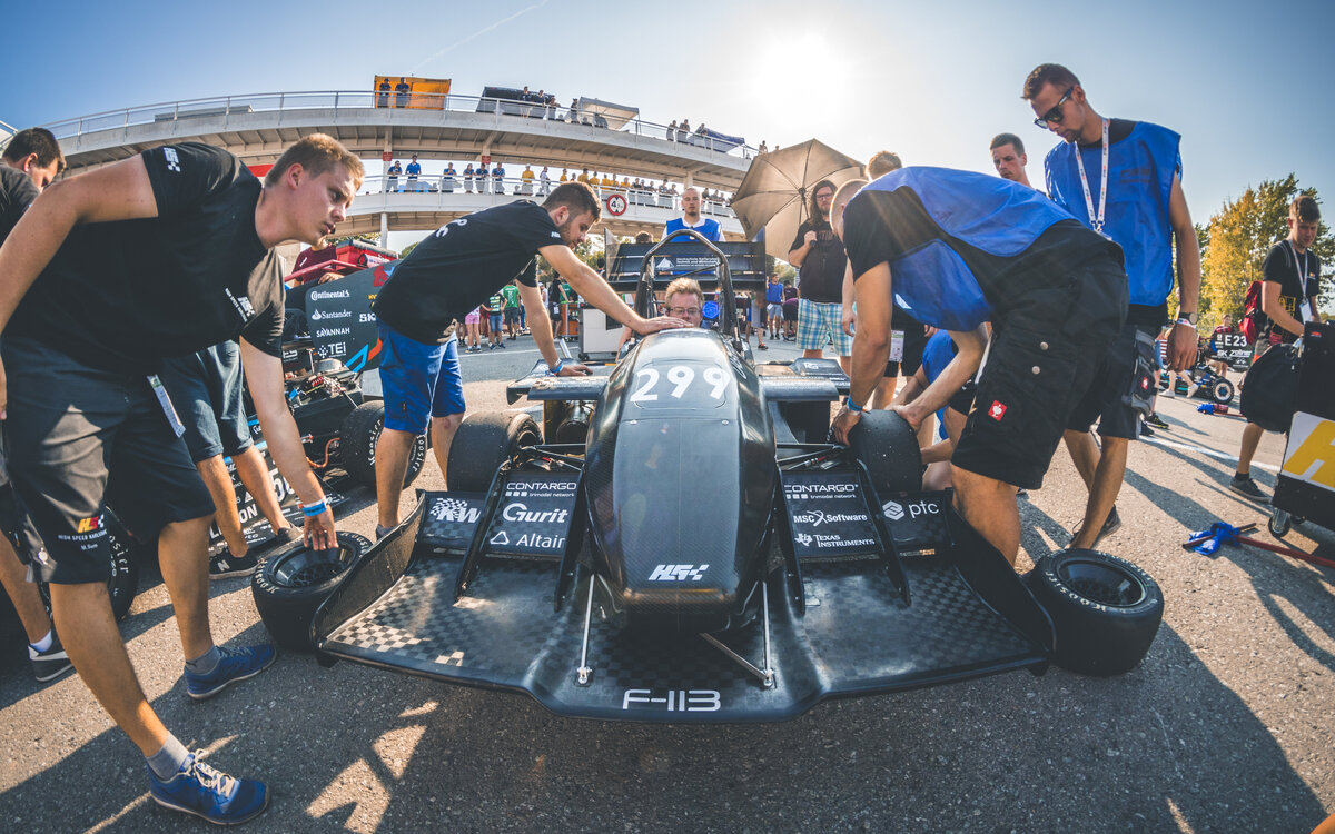 group of students gathered around the car and its pilot on the racecourse