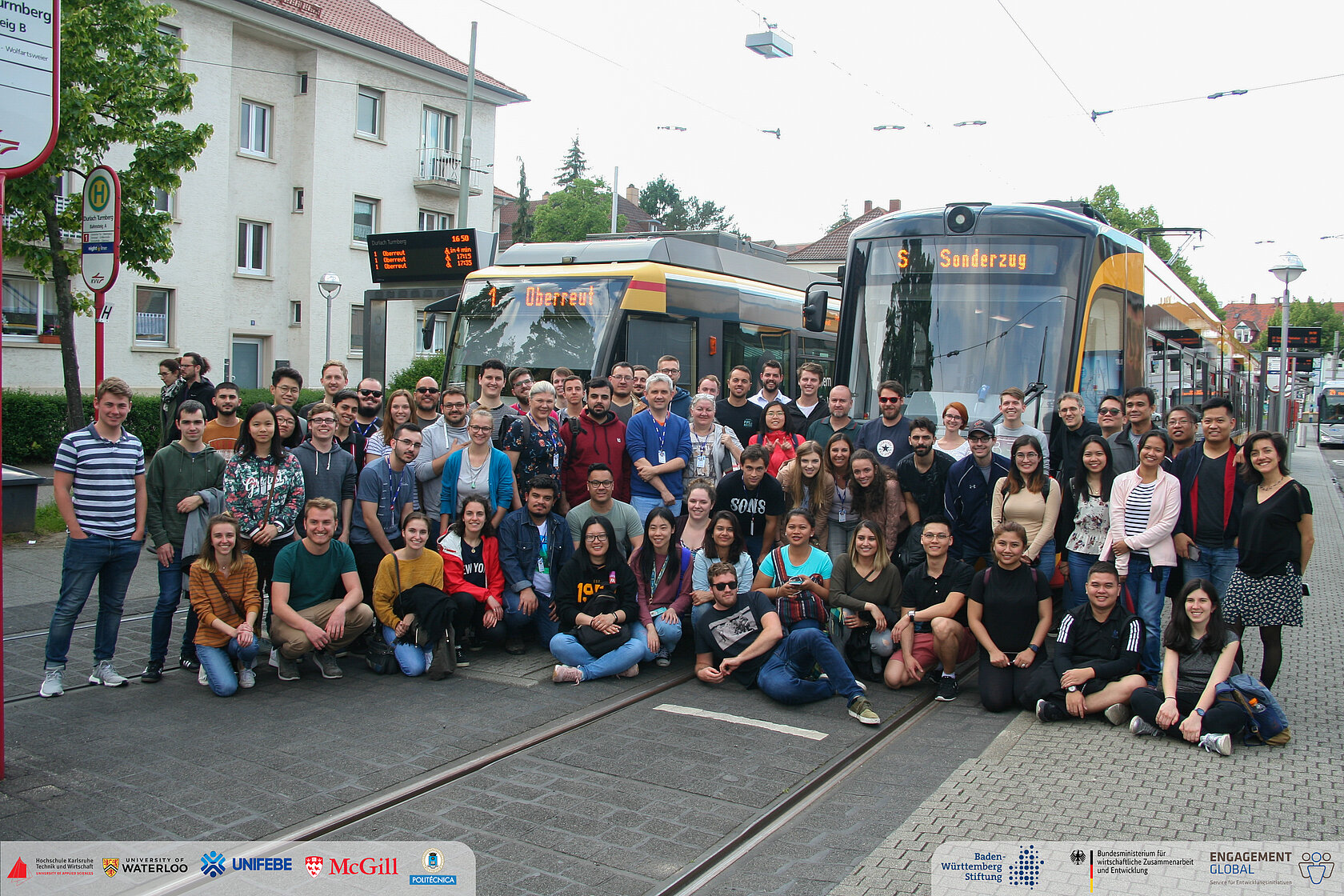 international group of students sitting in front of two trams