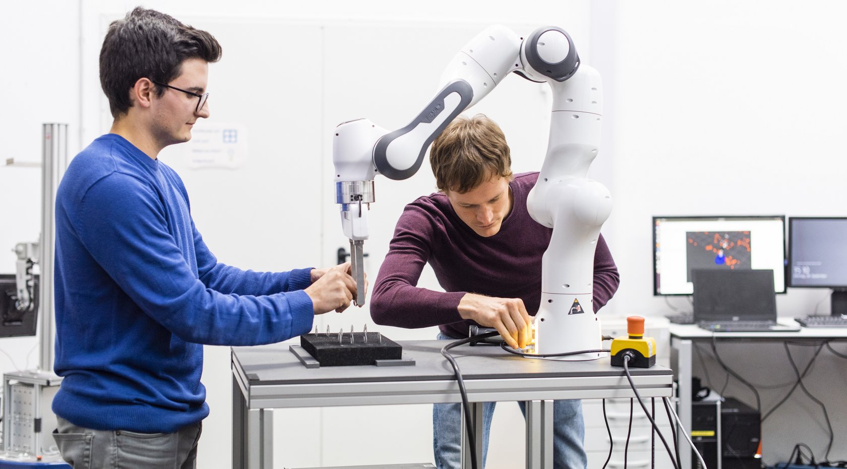 two students working on an industrial robot mounted on a table in the lab