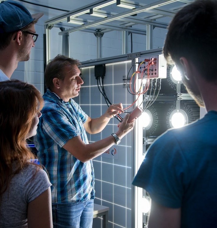 Professor und Studis arbeiten an einem Photovoltaik-System. Es ist ein Solar-Panel, das im Labor Erneuerbare Energien eingesetzt und weiterentwickelt wird.