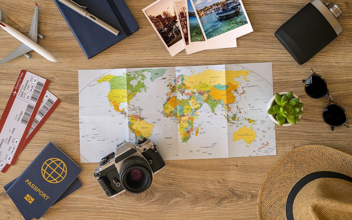 table strewn with map, passport, tickets, model airplane, camera and snapshots, sunhat, flask, and scrapbook 