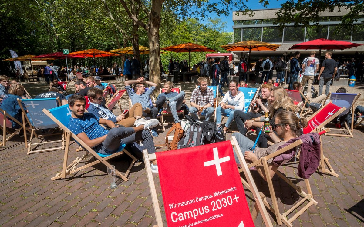 students sitting on deck chairs underneath umbrellas on campus