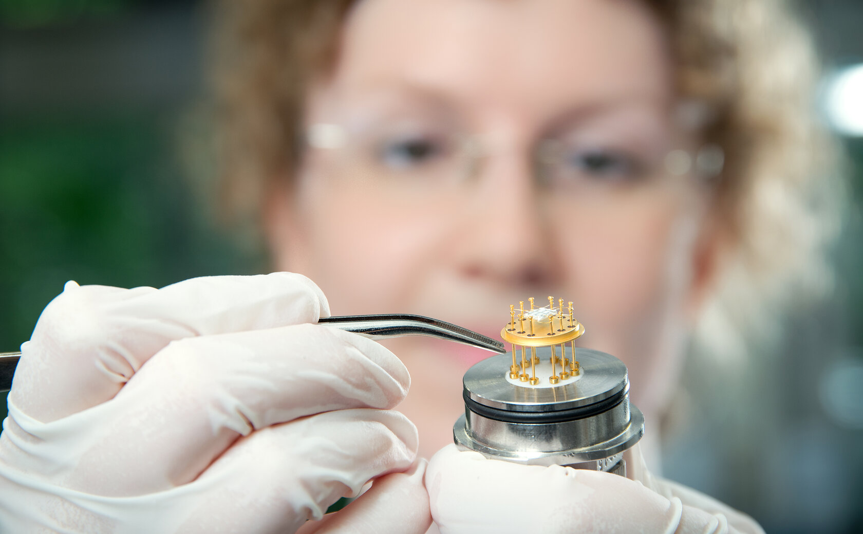 close-up of gloved hand holding a small sensor, with female face in the background