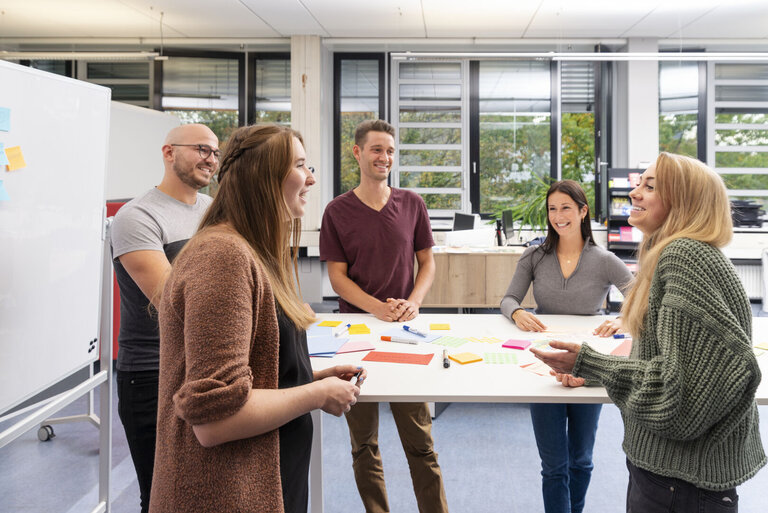 Fünf Menschen unterhalten sich an einem Stehtisch. 