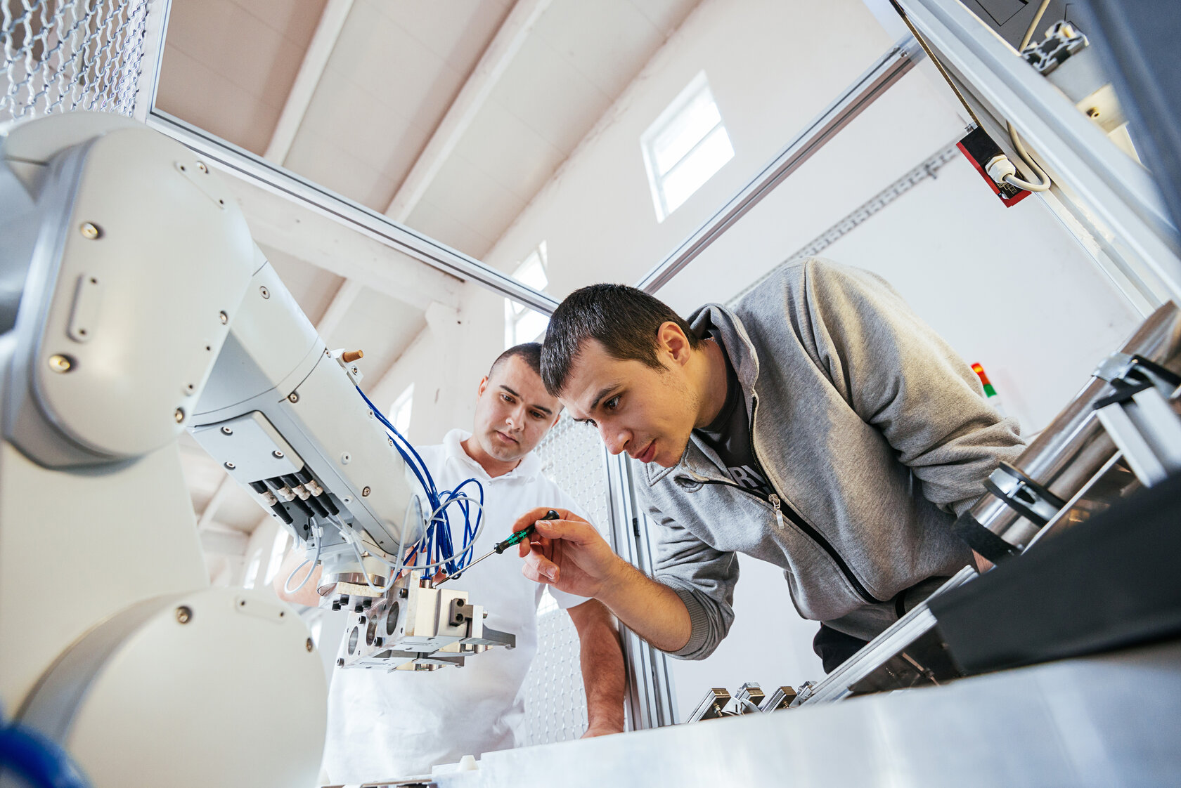 student adjusting an industrial robot, with second student looking on student adjusting an industrial robot, with second student looking on